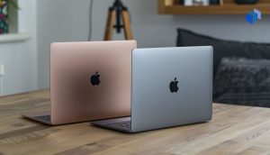 Två MacBook-datorer, en rosa och en silver, står på ett träbord för att representera jämförelsen av Macbook Air och Pro.