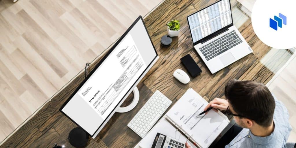 Overhead pic of man at desk with desktop, laptop and bunch of docs.