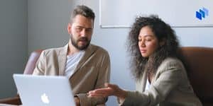 Two people sitting at a desk looking at a shared laptop