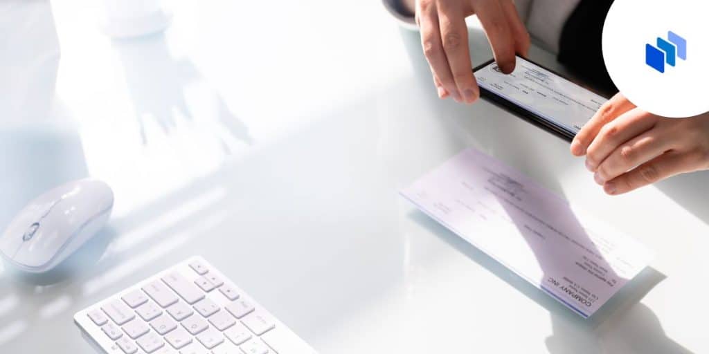 Image of someone holding a cheque above a desk with a keyboard in the background.